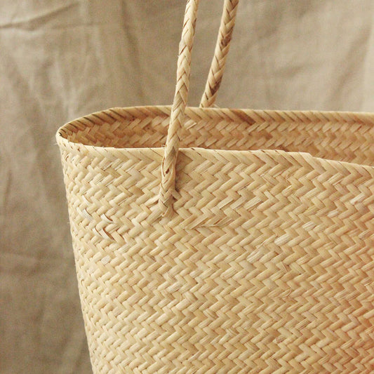Handwoven straw beach bag made from natural rattan, featuring pom-poms and tassels.